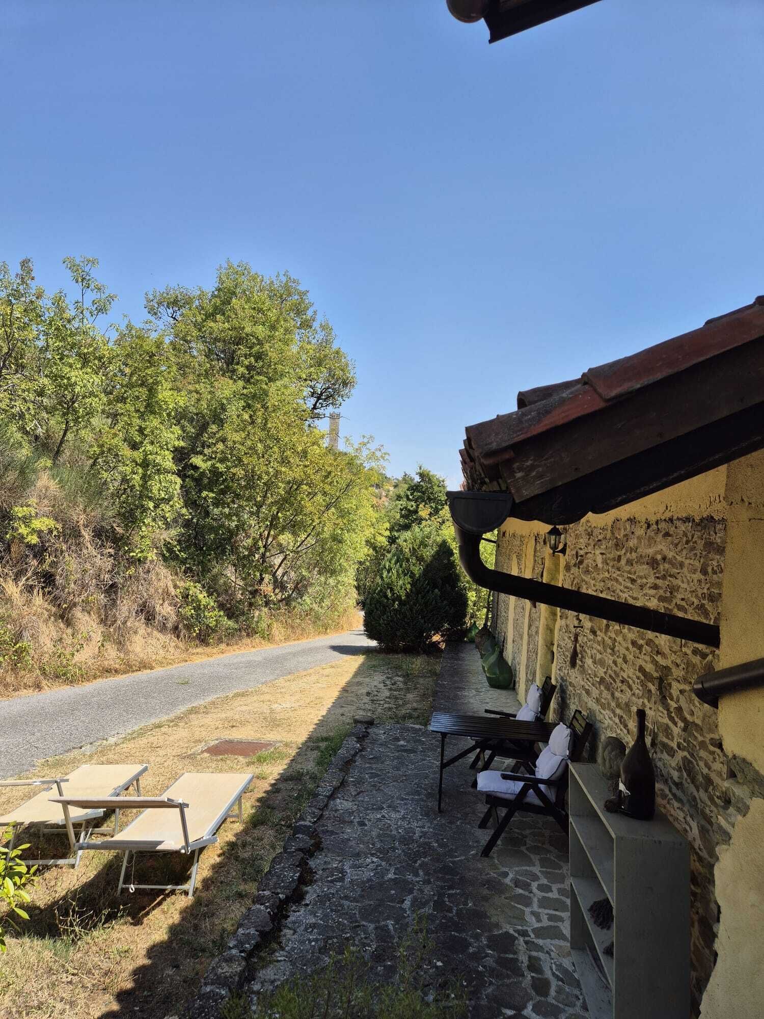 Un patio de piedra con mobiliario exterior, una carretera y una ladera boscosa.