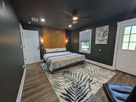 Quarto com cama, ventilador de teto, janela com persianas e porta.