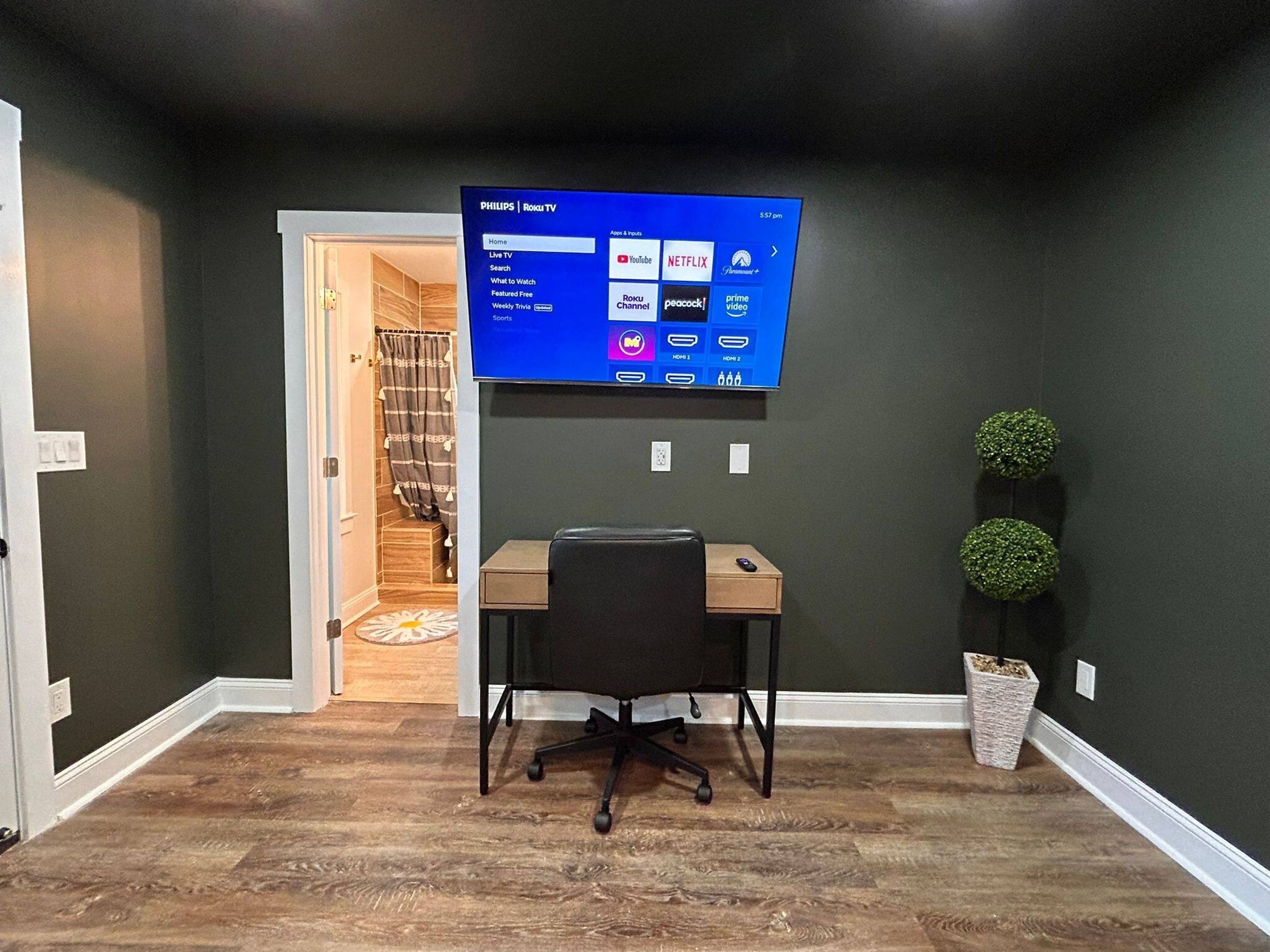 A home office with a flat-screen TV mounted on the wall, a desk, and a chair.