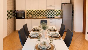 Eine moderne Küche mit weißen Schränken, einer karierten Spritzschutzwand und einem Essbereich für vier Personen mit einem weißen Tisch und Stühlen.