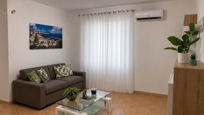 Ein Wohnzimmer mit einer Couch, einem Glastisch, einem Gemälde und einer Klimaanlage.