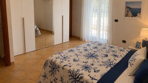 Ein Schlafzimmer mit einem Bett, einem Kleiderschrank, einem Fenster mit Vorhängen und einem Bild an der Wand.