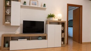 Ein modernes Wohnzimmer mit einem Flachbildfernseher, Holzregalen und einer durch eine offene Tür einsehbarer Küche.