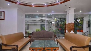 A room with two sofas, a table, and a glass wall with a view of the outside. - Hotel Kabeer New Delhi Railway Station  (New Delhi)