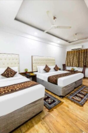 A hotel room with two beds, a ceiling fan, and a wooden floor. - Hotel Kabeer New Delhi Railway Station  (New Delhi)