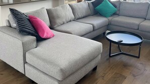 Una sala de estar moderna con un sofá seccional gris, una mesita de centro redonda y una cocina con armarios blancos y encimera negra.