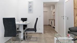 A modern, well-lit room with a dining table, two chairs, a glass coffee table, and a sofa. A kitchen area is visible in the background. - Stylish 1BR Studio In Central Vienna (Vienna)