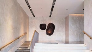 A modern staircase with marble steps and wooden handrails, leading to a landing with a unique wall art installation. - 45 Antasari Suite powered by Cocotel (Jakarta)