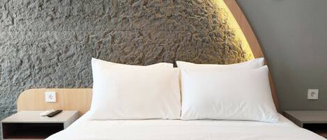 A bed with white linens, a wooden headboard, and a stone-textured wall behind it.