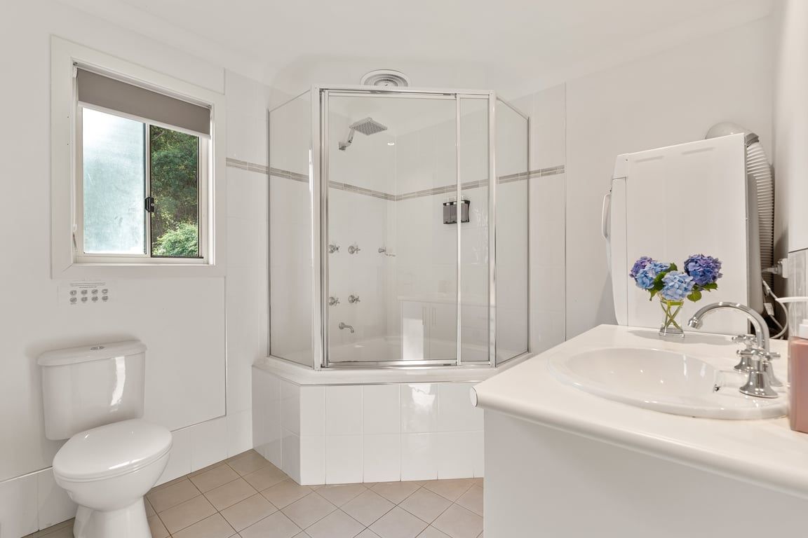 A bathroom with a shower enclosure, toilet, sink, and a window with a view of greenery.