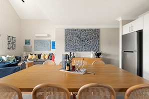 A modern kitchen with a dining area, featuring a large wooden table, chairs, and a refrigerator.