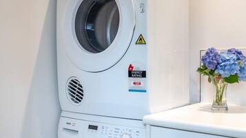 A stacked washer and dryer unit with a control panel, a warning label, and a small vase with flowers on top.