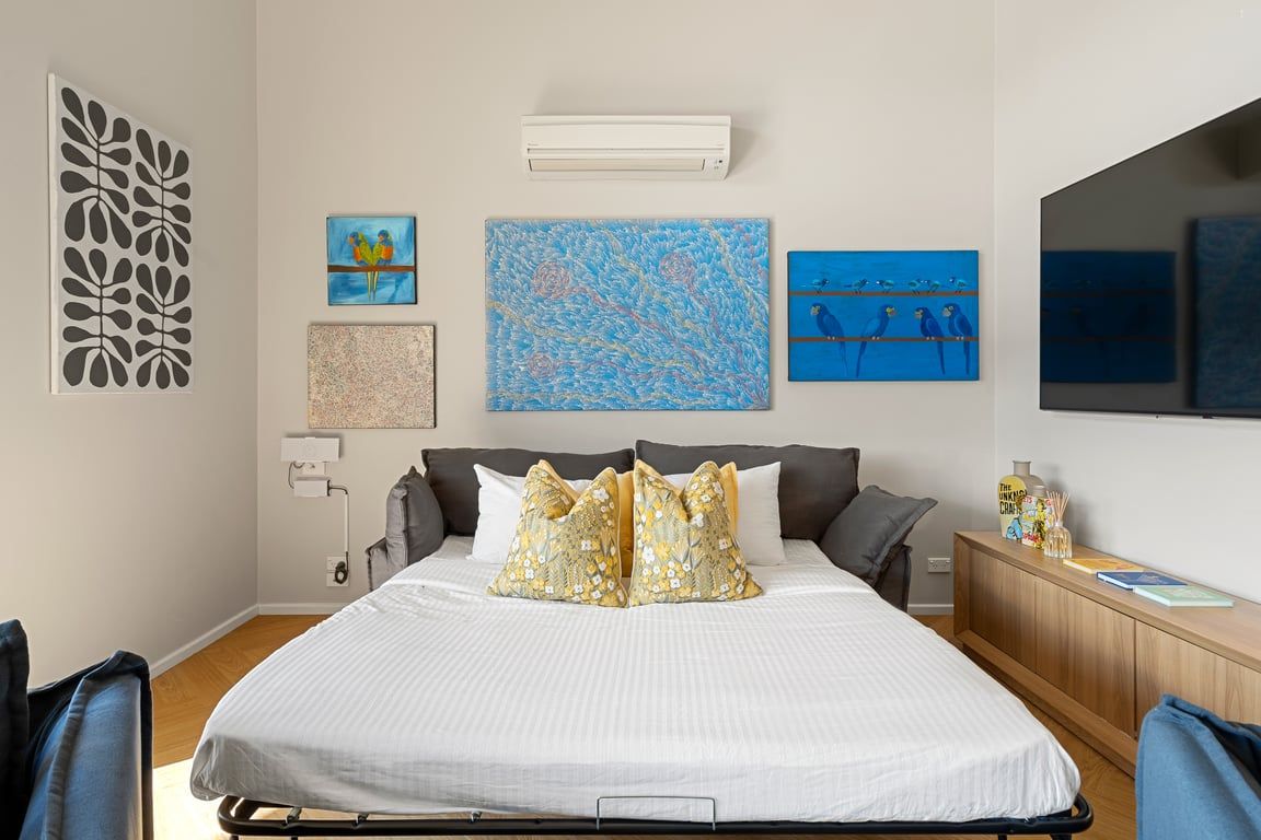Quarto com cama, travesseiros, mesa de cabeceira, abajur e quadros na parede.