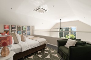 A bedroom with a bed, a green sofa, a window with a view, and wall art.