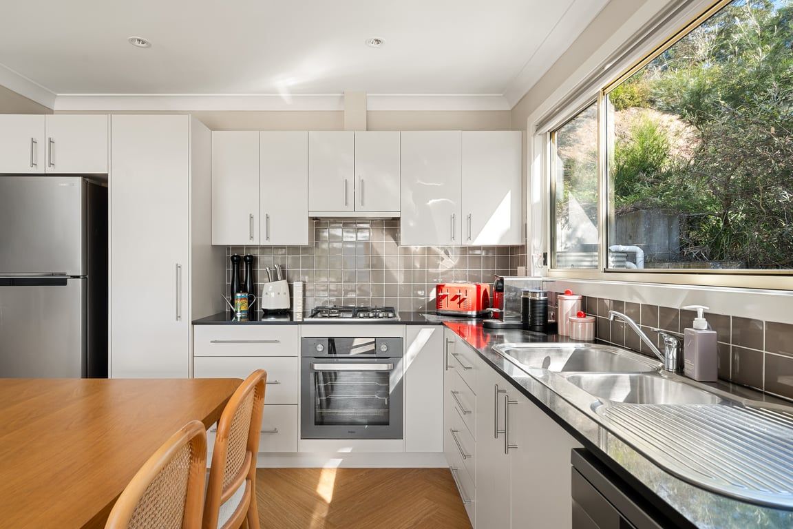 A modern kitchen with white cabinetry, a stainless steel refrigerator, a gas stove, and a large window providing a view of the outdoors.