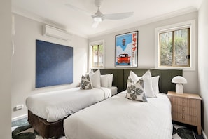 A hotel room with two beds, a ceiling fan, a framed picture, and a window with a view of greenery. - George's - Cabin 72 Kangaroo Valley Golf Course. Kangaroos, Wombats and Wildlife at your front door! (Kangaroo Valley)