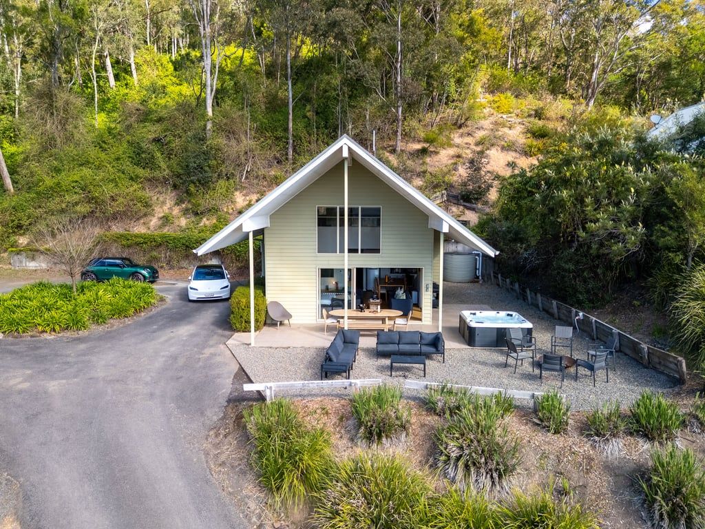 Uma casa de dois andares com área de pátio, banheira de hidromassagem e entrada para carros com dois veículos estacionados.