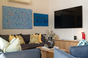 A living room with a sofa, a coffee table, a flat-screen TV, and artwork on the wall. - George's - Cabin 72 Kangaroo Valley Golf Course. Kangaroos, Wombats and Wildlife at your front door! (Kangaroo Valley)