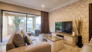 A modern living room with a large flat-screen TV, a sofa, a coffee table, and a sliding glass door leading to a patio. - A spacious, private home tucked just moments from Umhlanga’s coastline. (Durban)