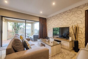 Ein modernes Wohnzimmer mit großem Flachbildfernseher, einer Couch, einem Couchtisch und einer Glastür, die auf eine Terrasse führt.