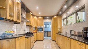A modern kitchen with wooden cabinets, stainless steel appliances, and a tiled floor. - A spacious, private home tucked just moments from Umhlanga’s coastline. (Durban)
