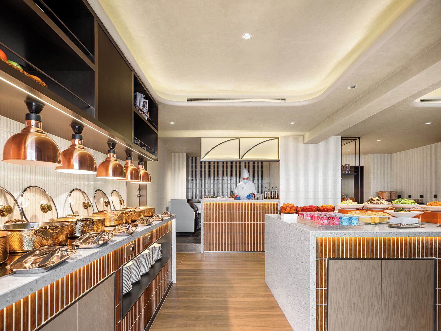 A modern kitchen with a central island, copper pendant lights, and a chef at work.