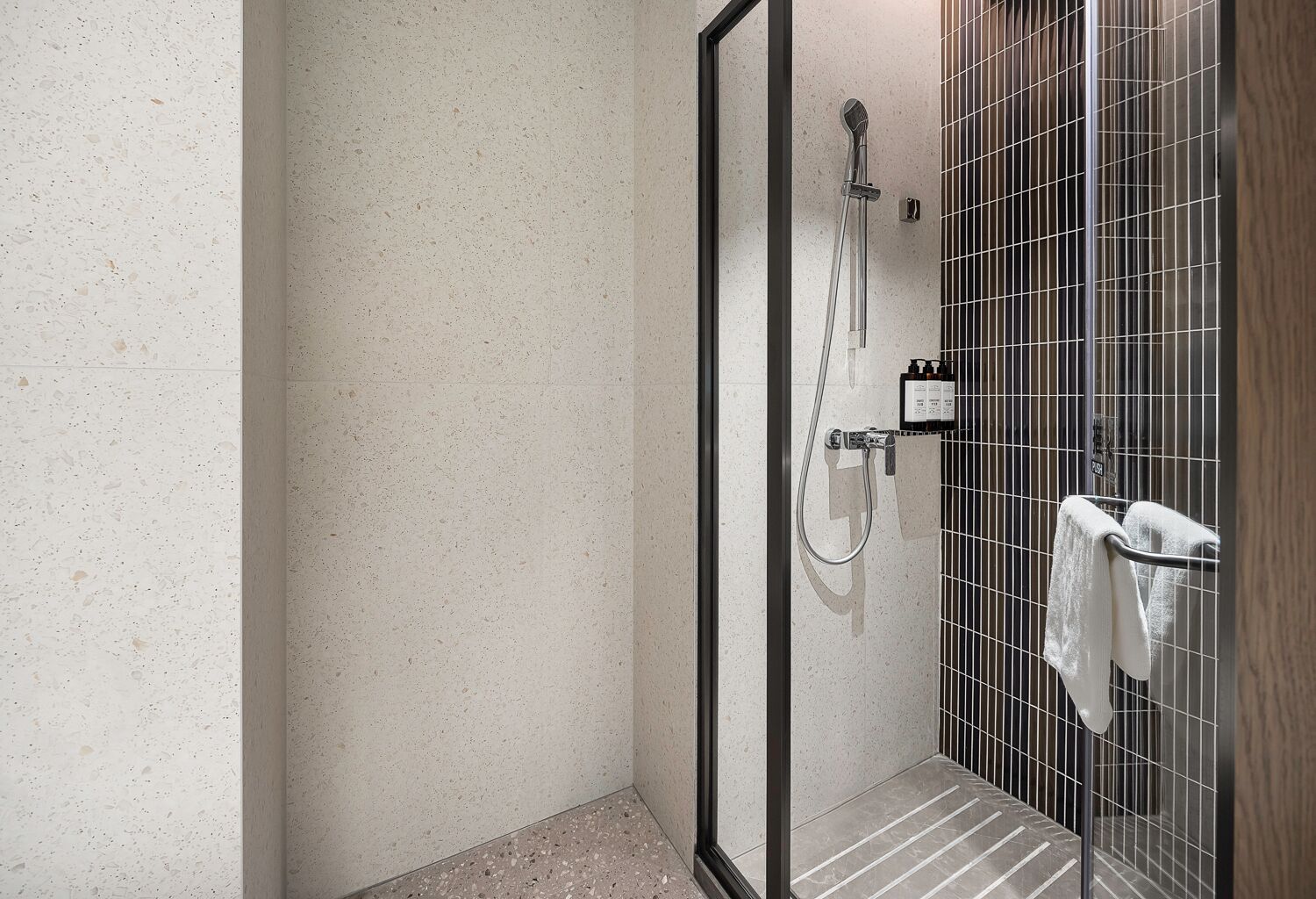 A modern shower area with a glass door, a handheld showerhead, and a towel rack with a towel.