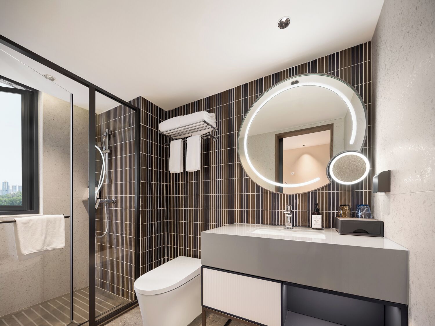 Un baño moderno con cabina de ducha de vidrio, inodoro, tocador con espejo y un perchero para toallas.