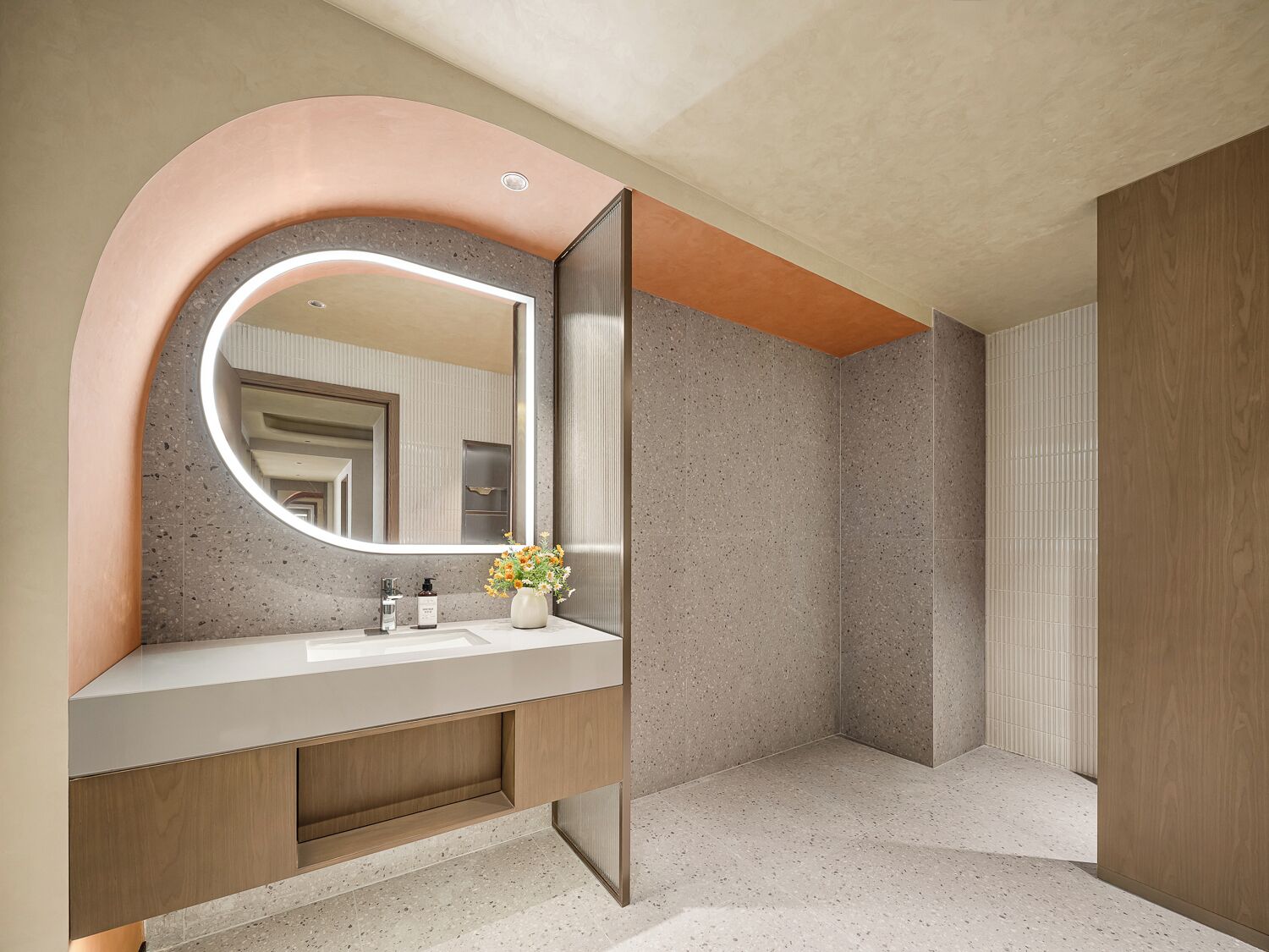 A modern bathroom with a curved mirror, a sink, and a vase with flowers.