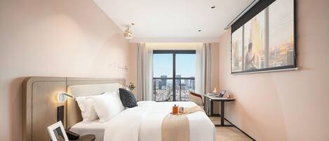 A modern hotel room with a large bed, bedside table, and a desk with a chair.
