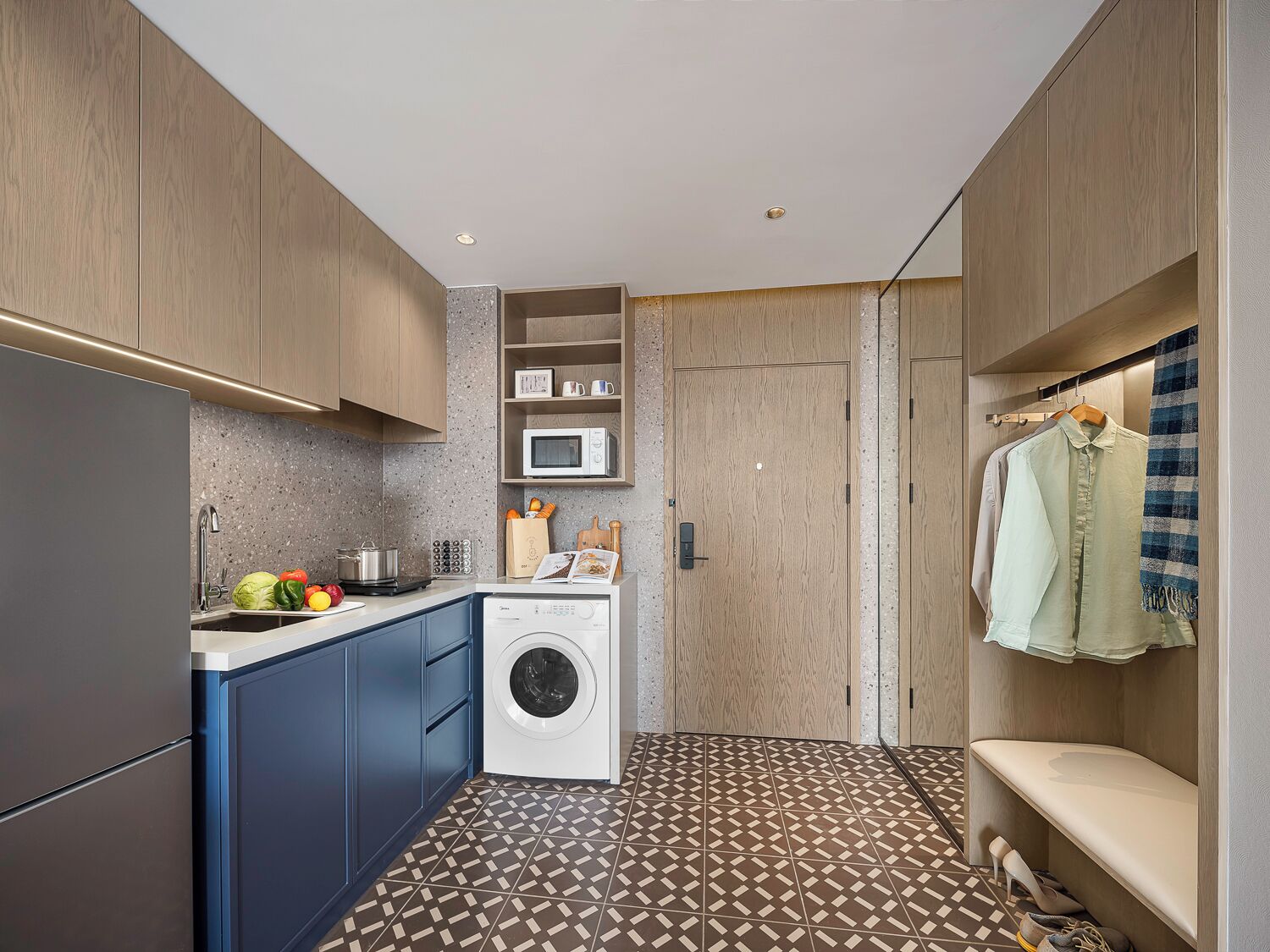 A compact kitchen with a washing machine, microwave, and a small countertop with fruits and vegetables.