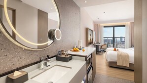 Un cuarto de hotel con un espejo grande, un espejo redondo, una cama, un escritorio y vistas de la ciudad.