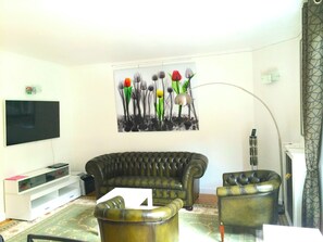 Una sala de estar con un televisor de pantalla plana grande, un sofá de cuero verde oscuro, un sillón a juego y una mesa de centro.