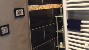 A bathroom with dark tiles, a white towel rack, and framed pictures on the wall.