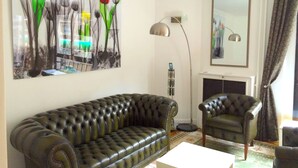 A living room with a tufted leather sofa, a matching armchair, a floor lamp, and a painting of flowers on the wall.
