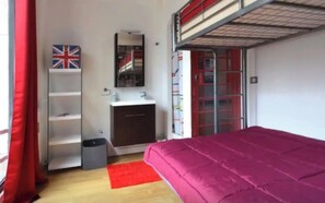 Una habitación pequeña con una cama litera, un escritorio, un espejo, un estante y una alfombra roja.