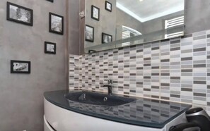 Un baño moderno con un lavabo de vidrio, salpicadero de azulejos y cuadros enmarcados en la pared.