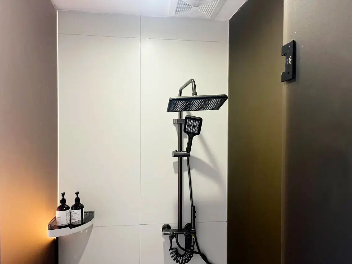 Un baño moderno con ducha, un pequeño estante con artículos de aseo y un interruptor de luz en la pared.