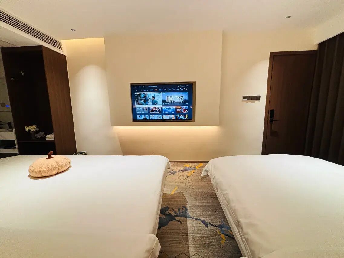 Une chambre d’hôtel avec deux lits, un téléviseur à écran plat fixé au mur et un sol recouvert de moquette.
