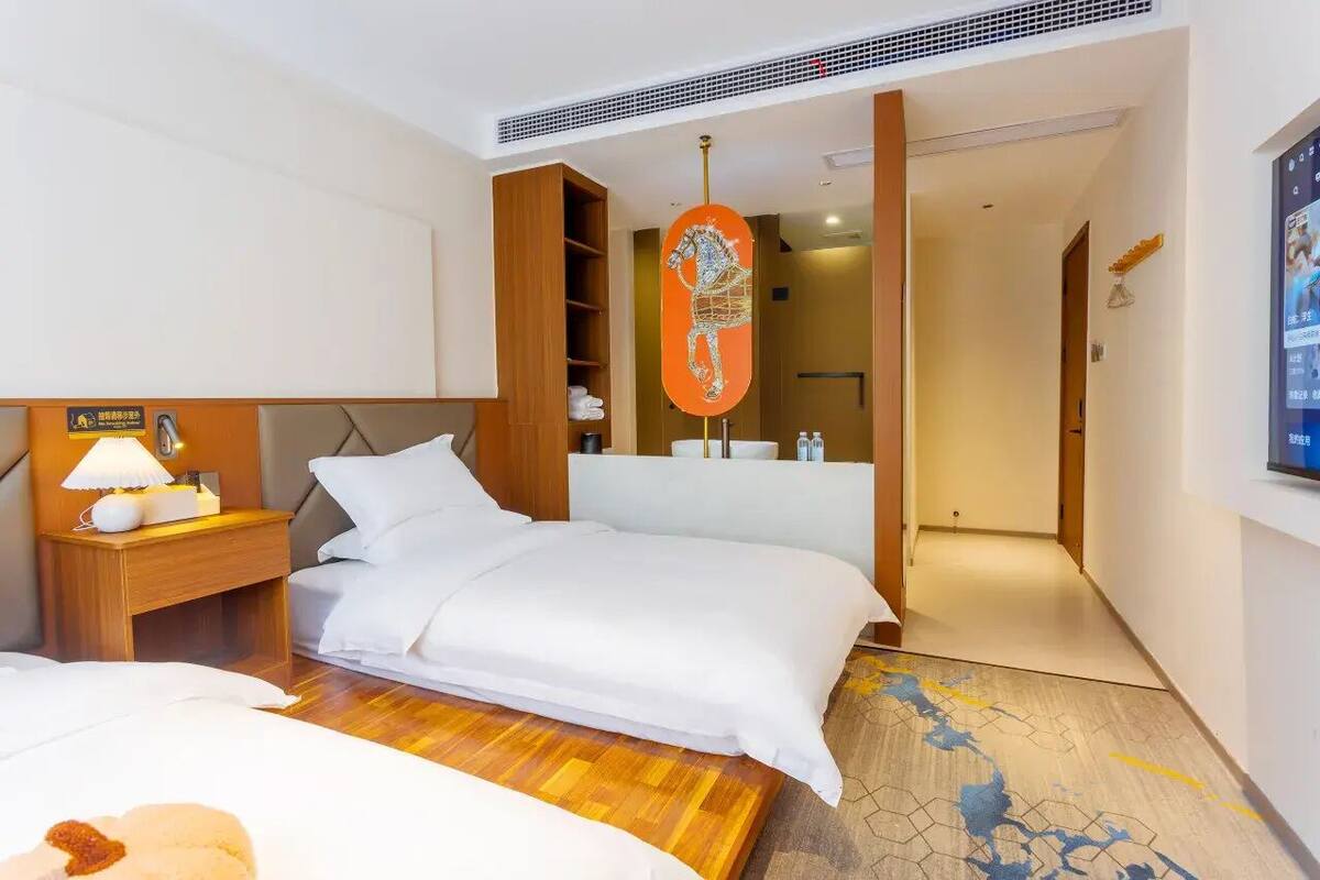 A hotel room with a bed, bedside table with a lamp, a wooden headboard, a mirror, and a decorative horse sculpture.