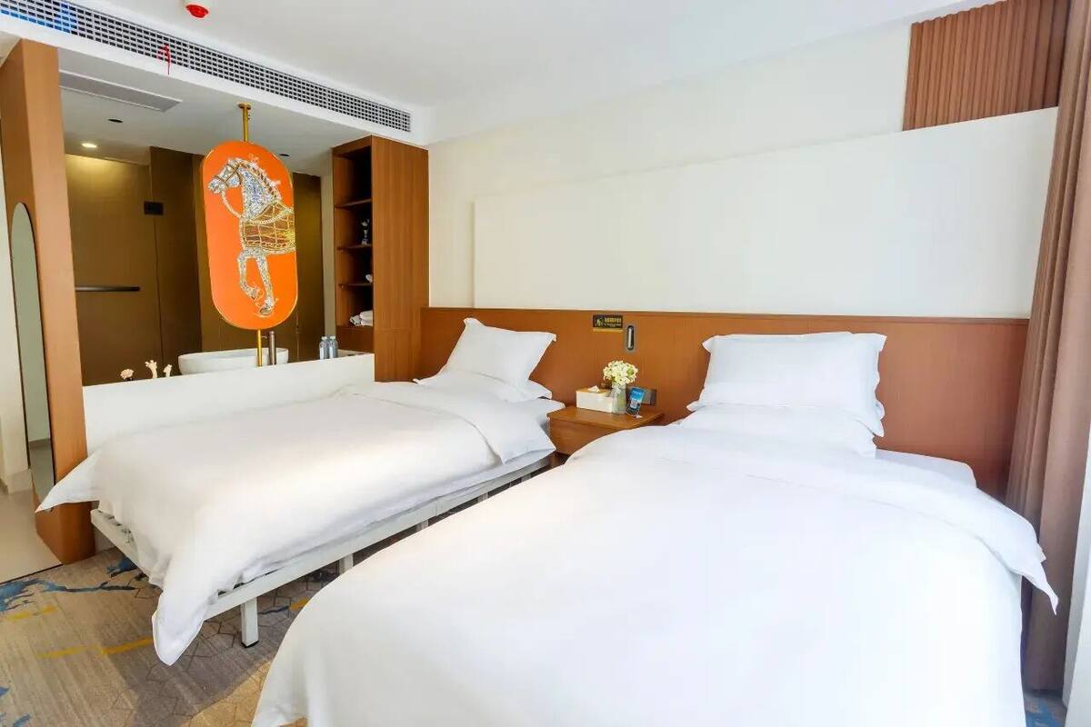 A hotel room with two beds, a wooden headboard, a nightstand with a lamp, and a decorative horse sculpture.