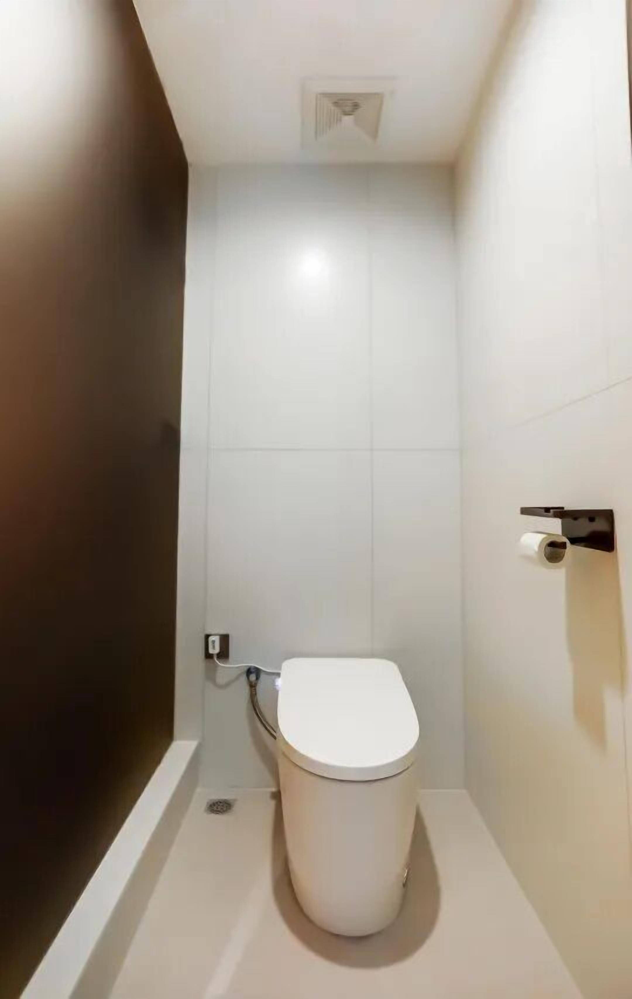 A small, modern bathroom with a toilet, a wall-mounted toilet paper holder, and a visible electrical outlet.