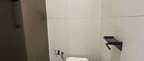 Et lille, moderne badeværelse med et hvidt toilet, en sort skraldespand og en sort hylde på væggen.