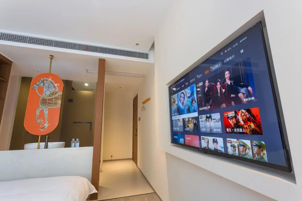 A hotel room with a large TV mounted on the wall displaying various content.