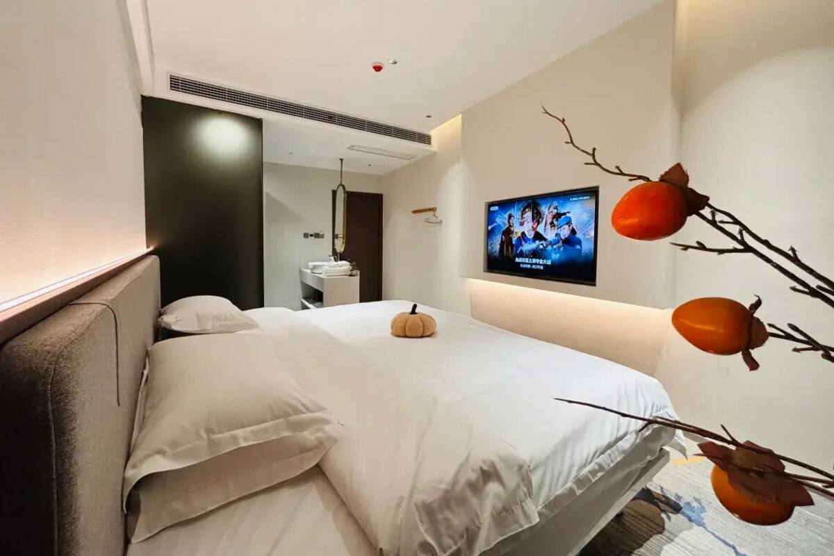 A modern hotel room with a large bed, a flat-screen TV mounted on the wall, and a decorative wall art piece.