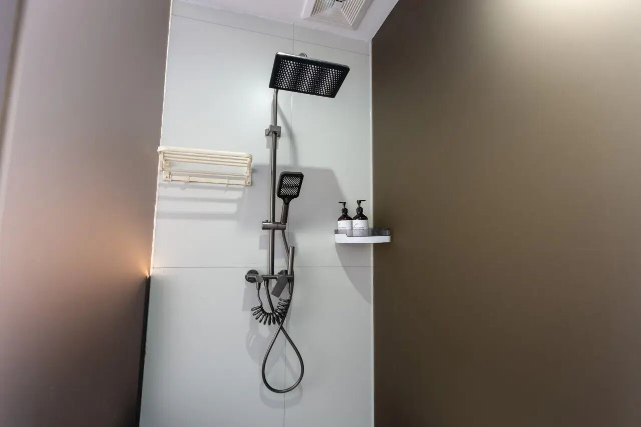 A modern bathroom with a wall-mounted shower, a towel rack, and a soap dispenser.