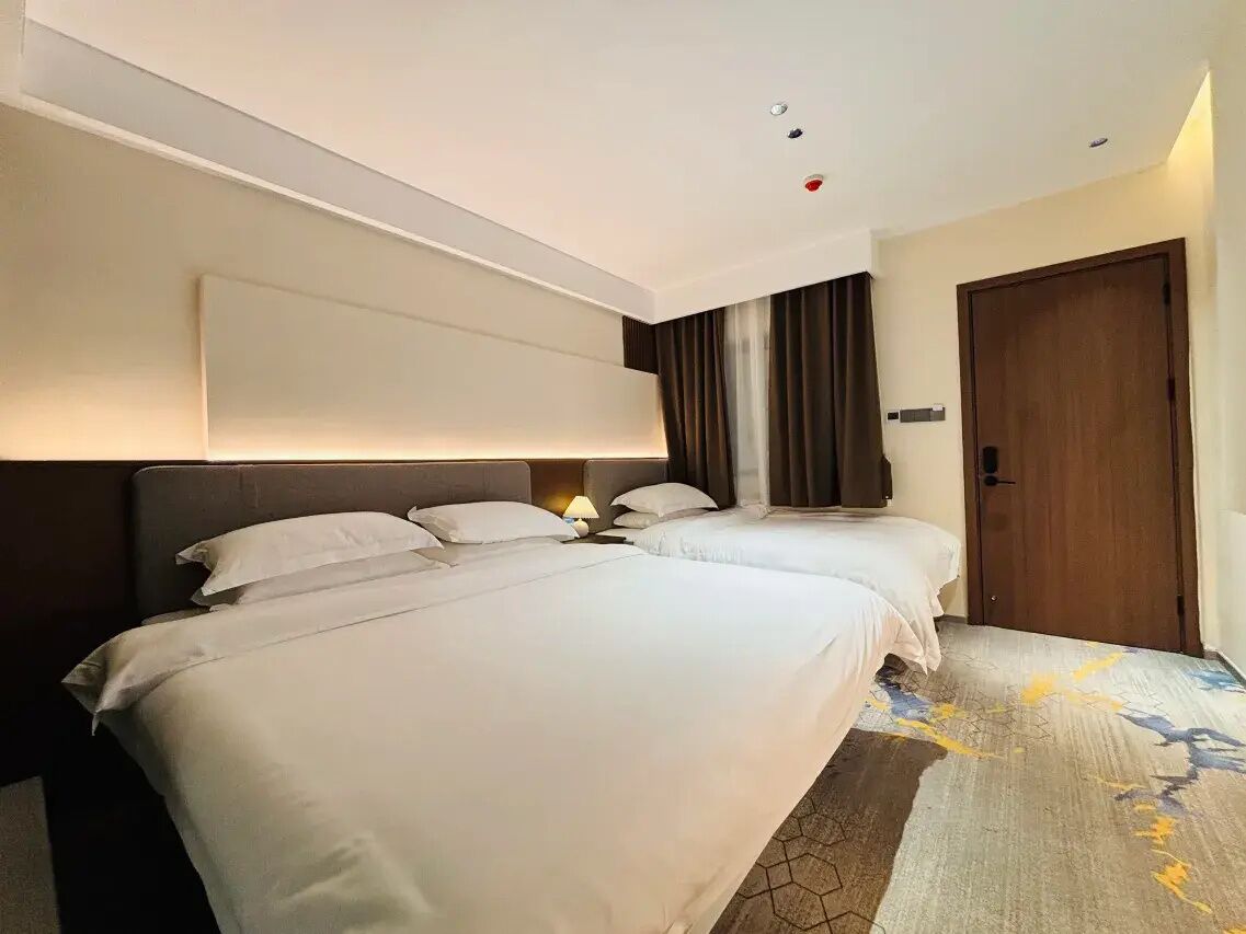 A hotel room with two beds, a wooden door, and a patterned carpet.