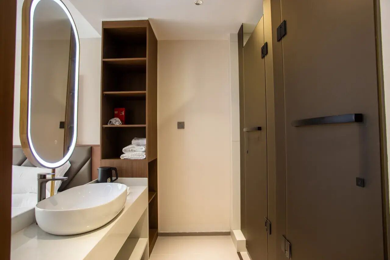 A modern bathroom with a large oval sink, a round mirror, and a built-in shelf with towels.