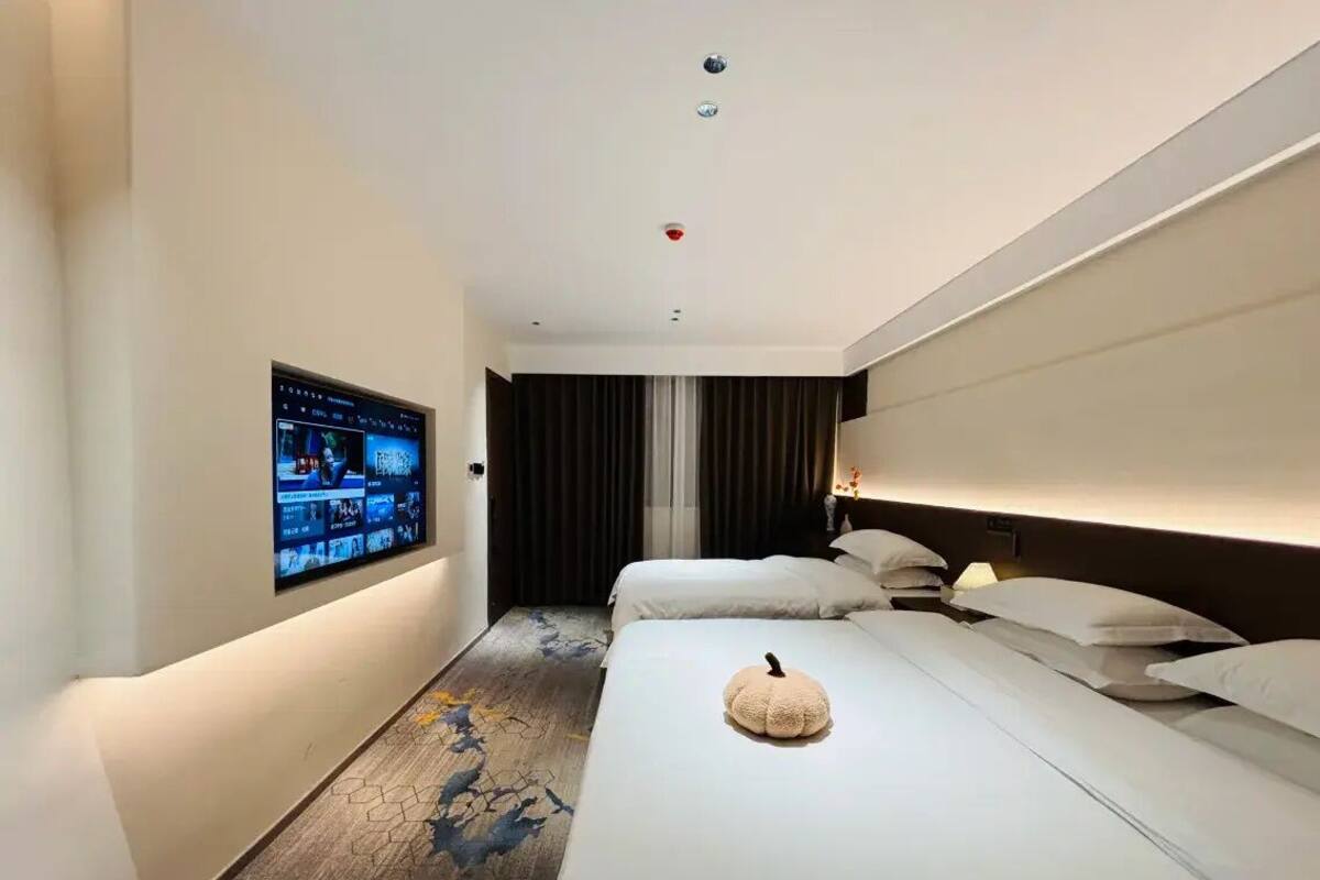 A hotel room with a large bed, a flat-screen TV mounted on the wall, and a small decorative pumpkin on the bed.