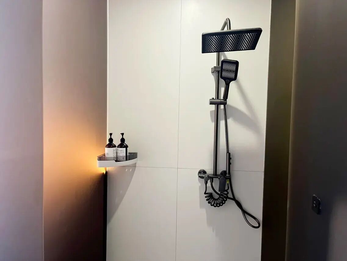 Un baño moderno con ducha empotrada, cabezal de ducha de mano y dispensador de jabón en un estante pequeño.